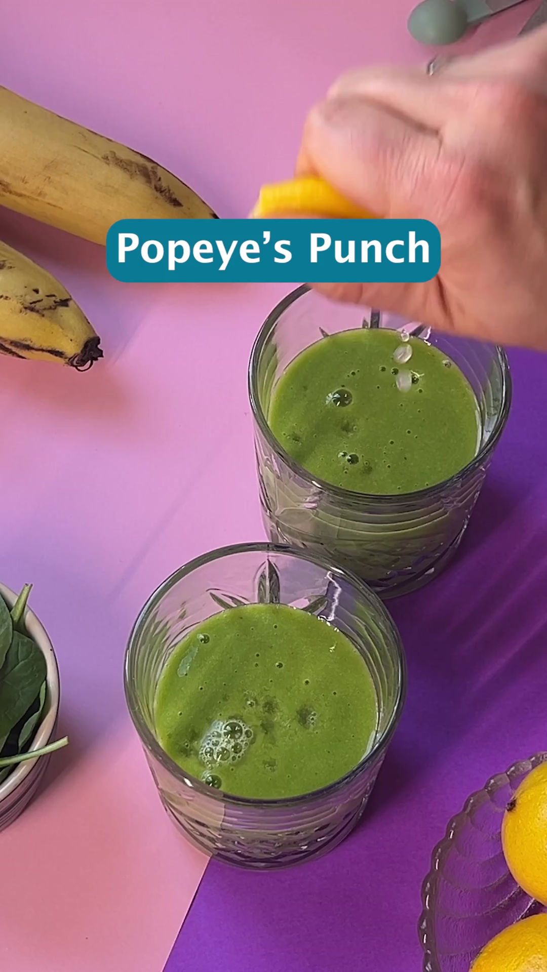 two short glasses with a green smoothie. A hand squeezes lemon into one of the glasses