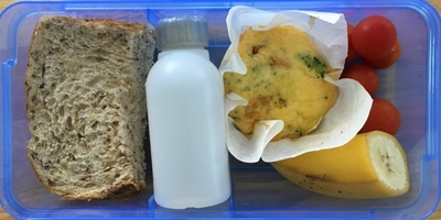A plastic lunchbox with a wholemeal sandwich, mini frittata, cherry tomatoes, half a banana and a small reusable water bottle