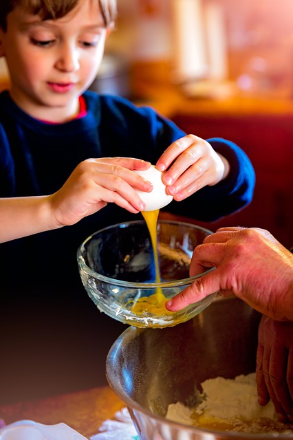 Child cracking an egg into a bowl with an adult helping