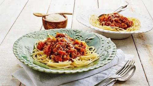 Bowl of spaghetti with tomato sauce and vegetables on top.