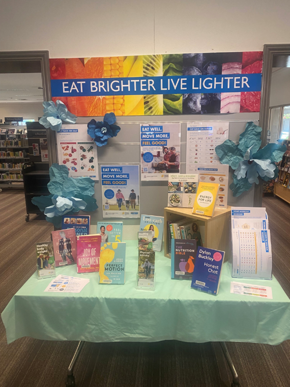LiveLighter resources displayed on a table in a library with a sign in the background saying Eat Brighter Live Lighter