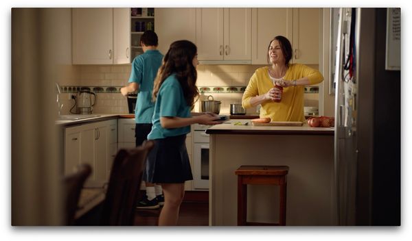Still from the Menu App television advert showing a mother in the kitchen opening a jar of pasta sauce. Her two high school aged children are in the kitchen helping.