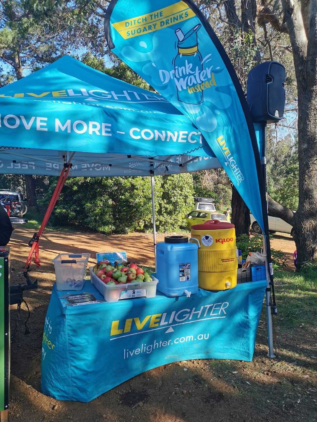 Marquee with with LiveLighter branding set up in a bush setting. On the table is a crate of apples and several water containers. Signage says 'Drink the sugary drinks. Drink water instead.'