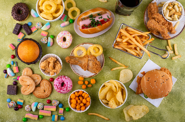 Display of different types of ultraprocessed foods including lollies, crisps, hot chips, hot dog, fried chicken, burger, donuts, cheese balls and pastries.