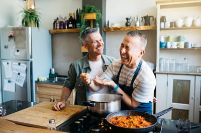Two men cook dinner while laughing