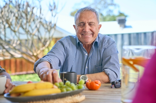 Man sitting at a table reaches forward to pick up a piece of fruit off a fruit platter in front of him.
