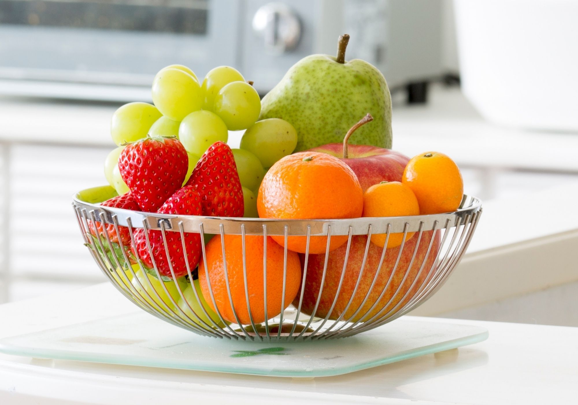 Wire basket on a kitchen bench containing grapes, strawberries, oranges, apple and pear