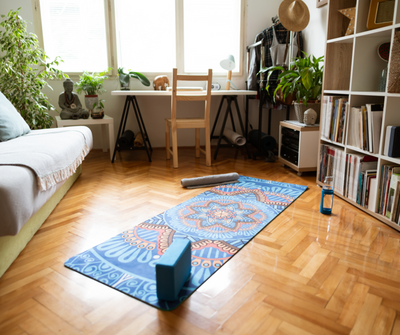 A yoga mat with a speaker, roller and water bottle on a living room floor