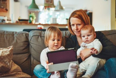 Woman looks at tablet with toddler and baby