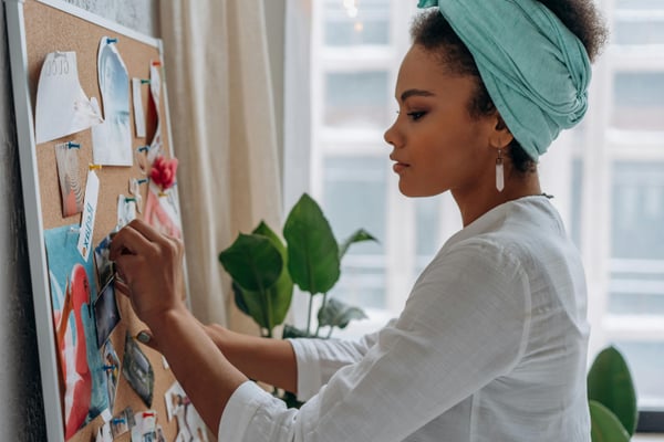 Woman looks at a cork board as she pins an item on it.
