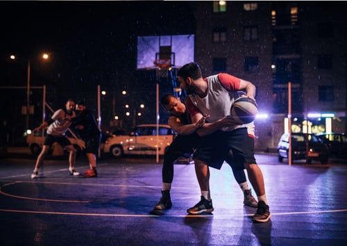Group of men play basketball at night in an urban area
