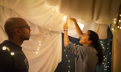 Man and woman string lights inside a blanket fort