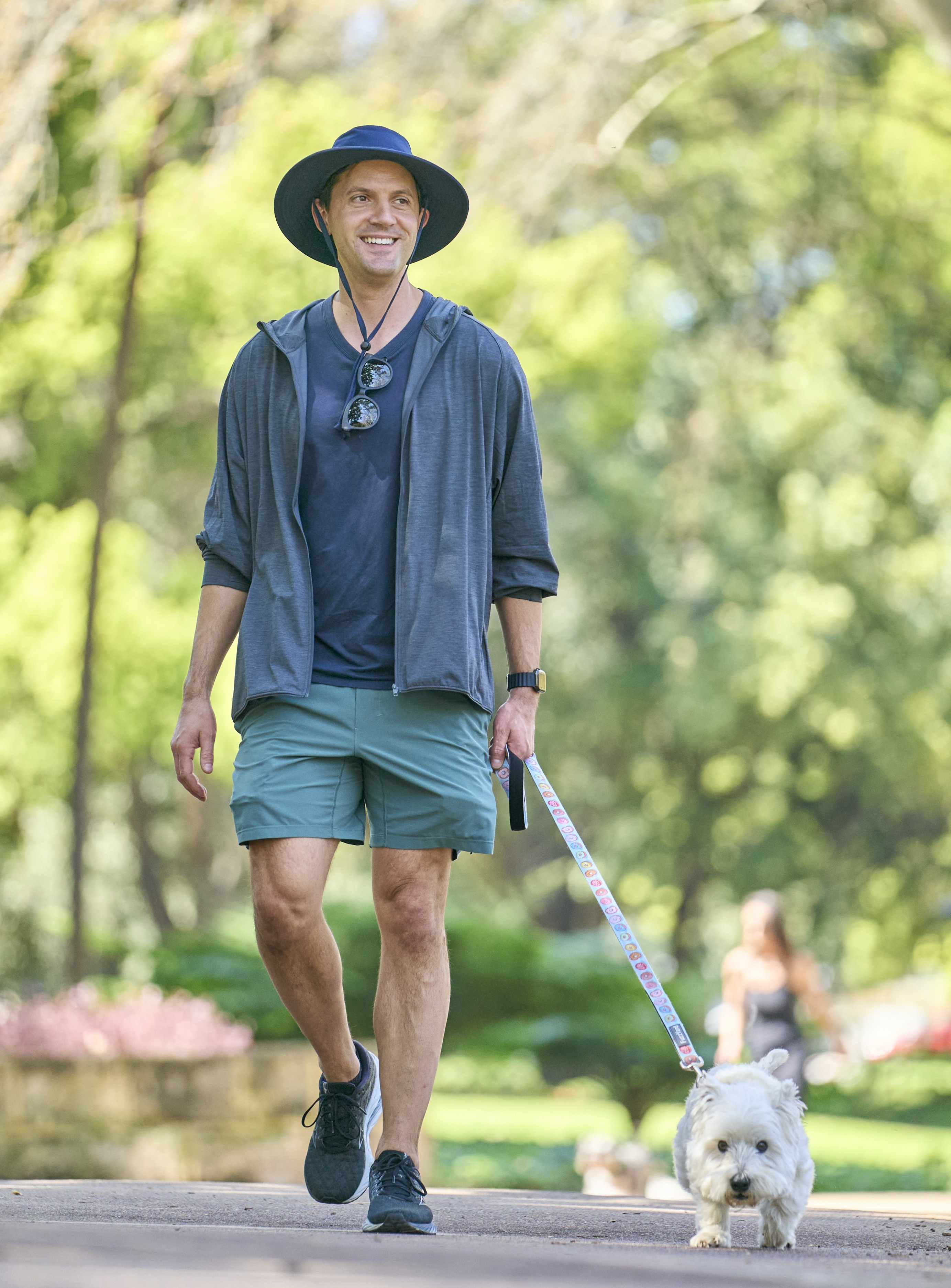 man walks dog in park wearing a hat