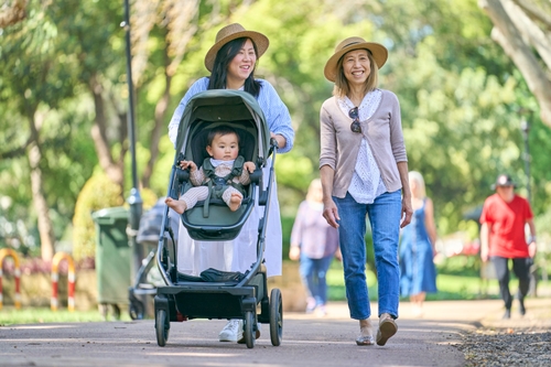 Two women walk in the park while pushing a pram