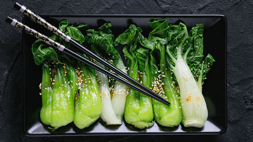 cooked bok choy and choy sum on a plate with sesame seeds 