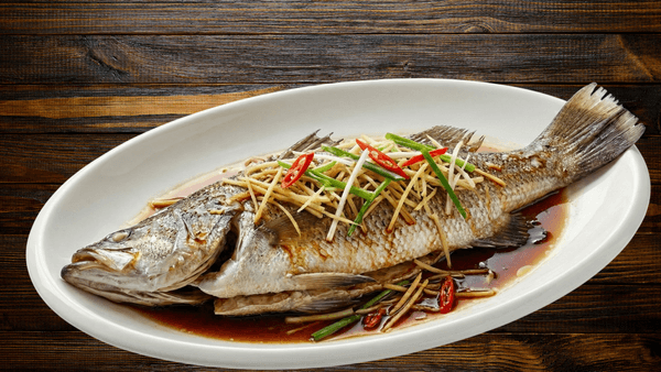 A plate with a whole cooked fish topped with shredded ginger, chilli and herbs. 