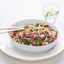 A chicken and slaw salad in a bowl with a glass of water in the background. 