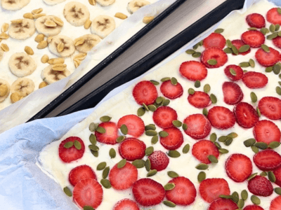 Two trays of frozen yoghurt bark; one with banana and peanuts, one with strawberries and pepitas