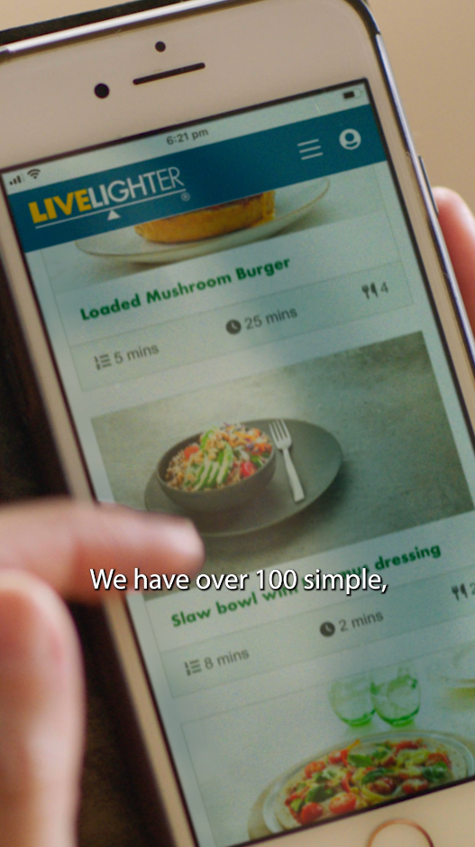 Still image from the menu app commercial, close up someone scrolling through their phone looking at LiveLighter recipes, close captions on the screen read 'we have over 100'