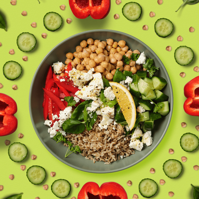 Overhead shot of a salad bowl with chickpeas, capsicum strips, fetta, brown rice, cucumber and a lemon slice. A kaleidoscope of the ingredients surrounds the bowl.