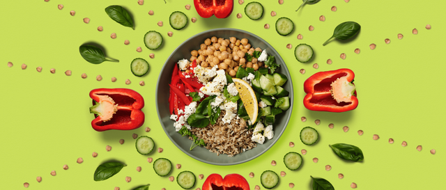 Overhead shot of a salad bowl with chickpeas, capsicum strips, fetta, brown rice, cucumber and a lemon slice. A kaleidoscope of the ingredients surrounds the bowl.
