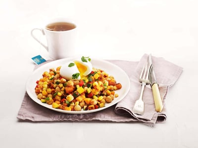 A delicious dish of diced and spiced vegetables like sweet potato and capsicum topped with a gooey boiled egg and served with a cup of tea. 