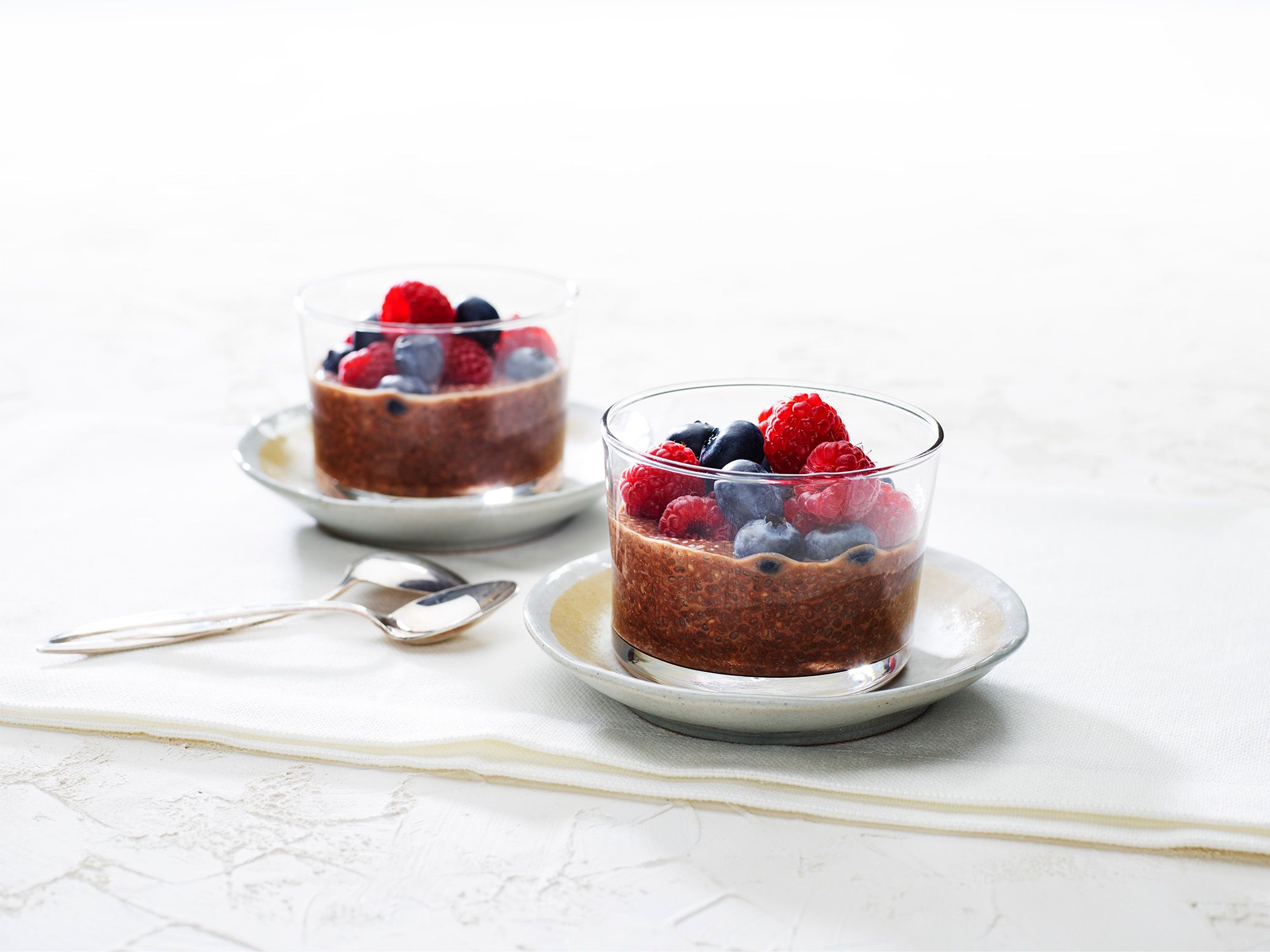 Two short glasses containing a chocolate coloured pudding topped with fresh blueberries and raspberries