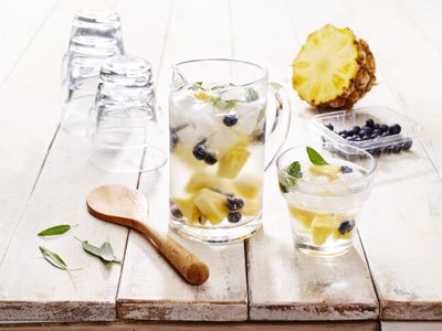 Glass jug filled with water, blueberries, mint, pineapple pieces and ice.