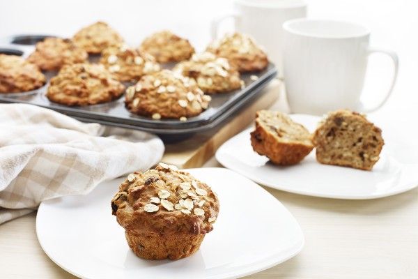 Small muffin with a sprinkle of oats on top. In the background is a muffin tin tray with more muffins inside.